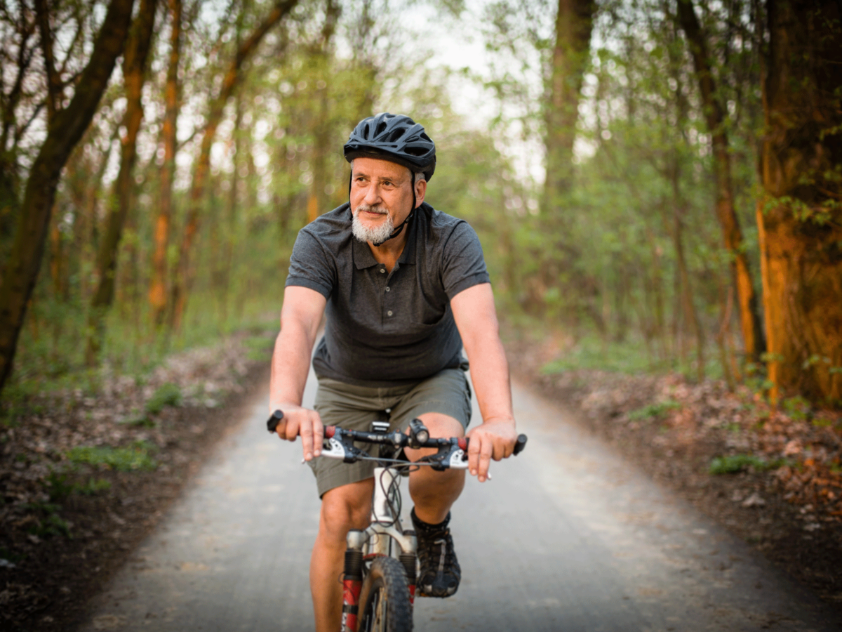 Oudere man op mountainbike op een weg in het bos